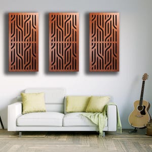 May include: Three rectangular wooden wall panels with a repeating, abstract, linear design in a warm brown color. The panels are mounted on a white wall above a white sofa with yellow pillows. A guitar and lamp are also in the room.