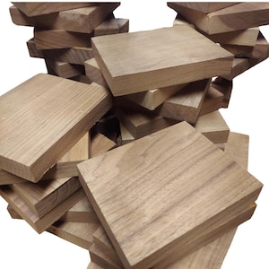 May include: A pile of unfinished, rectangular wooden blocks. The blocks are a light brown color with visible wood grain. The blocks are stacked and scattered, suggesting a supply of raw materials for woodworking or crafts.