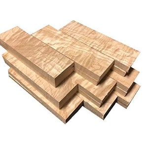 May include: A stack of light-colored maple wood blocks with a wavy grain pattern. The blocks are rectangular and appear to be freshly cut, with a natural wood tone. The wood is stacked in a staggered arrangement.