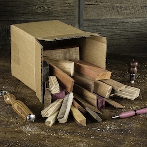 May include: A cardboard box overflowing with a variety of wood scraps in different colours and shapes. The wood scraps are arranged in a random pattern and appear to be ready for woodworking projects.
