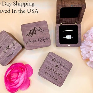 May include: Three wooden ring boxes with engraved text. The first box says "Jacob & Stelly The Scott February 14, 2024". The second box says "Amelia & Elyah" with a mountain range design. The third box says "Emily & Daniel 02.14.2024".