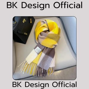 May include: A yellow and brown plaid scarf with fringe. The scarf is folded and draped over a chair.