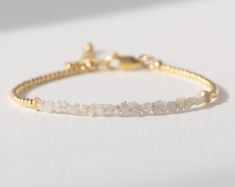 May include: A delicate gold bracelet featuring a row of small, rough-cut, light-colored gemstones. The bracelet has a thin, textured gold band and a secure clasp. The gemstones are the focal point, creating a subtle sparkle.