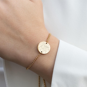 May include: A gold bracelet with a round charm featuring a delicate floral design. The bracelet is made of a thin chain and has a simple, elegant style.