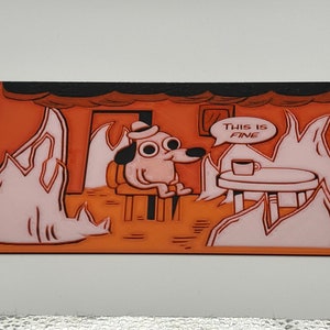 May include: A cartoon dog sits in a chair with a cup of coffee on a table in front of him. The dog is wearing a hat and has large, wide eyes. The room is on fire, but the dog says "This is fine" in a speech bubble above his head.