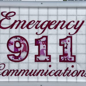 Puede incluir: Diseño bordado en tela blanca con las palabras "Emergency 911 Communications" en hilo rosa.
