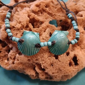 Op de afbeelding: Een turquoise blauwe schelp charme armband met zwart koord en turquoise blauwe kralen.