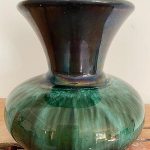 May include: A green and black ceramic vase with a flared opening and a rounded body. The vase has a glossy finish and a swirling pattern.