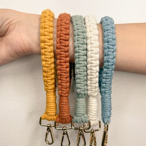 May include: Five colorful macrame straps with gold clasps. The straps are in shades of yellow, orange, green, white, and blue.