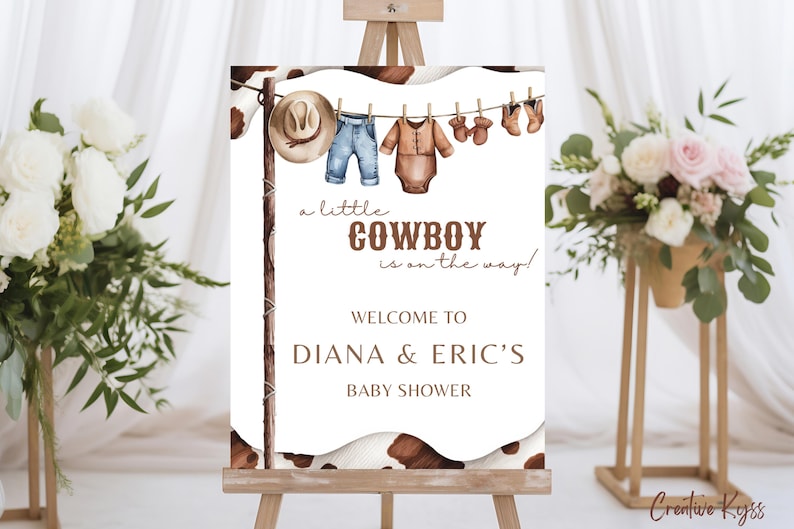 May include: A white sign with brown text announcing a baby shower for Diana & Eric. The sign says "a little COWBOY is on the way!" and features a line of baby clothes hanging on a clothesline, including a cowboy hat, jeans, a onesie, and booties.