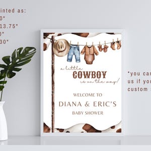 May include: A white framed printable sign with a brown cowhide background. The sign says "A little cowboy is on the way!" and "Welcome to Diana & Eric's Baby Shower". The sign also has a watercolor illustration of baby clothes hanging on a clothesline.