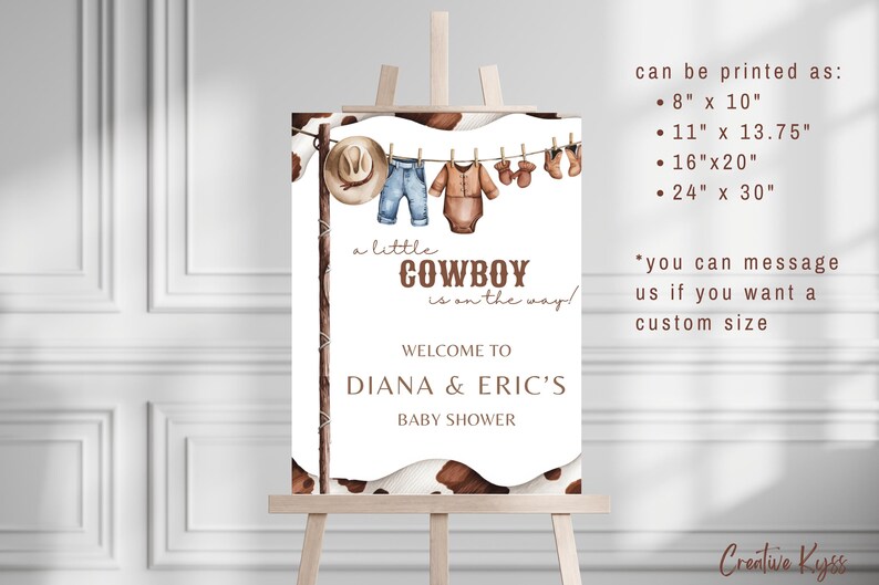 May include: A white sign with a brown cowhide pattern border. The sign says "a little COWBOY is on the way!" and "WELCOME TO DIANA & ERIC'S BABY SHOWER". There are illustrations of baby clothes hanging on a clothesline. The sign also includes information about printing sizes: 8" x 10", 11" x 13.75", 16" x 20", and 24" x 30".
