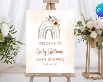Puede incluir: Un letrero de bienvenida para un baby shower, con un arcoíris de acuarela y decoraciones florales. El letrero dice "Welcome to Emily Williams Baby Shower 01.16.20xx" sobre un fondo melocotón claro, exhibido en un caballete de madera.