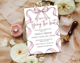 May include: A white bridal shower invitation with pink ribbon accents. The text reads "She's Tying the Knot" with the bride's name, date, time, and RSVP information.
