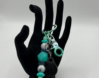 Colorful teal keychain with white and gray marbled  silicone beads and rhinestone spacers. Flashlight and green metal clip are included.