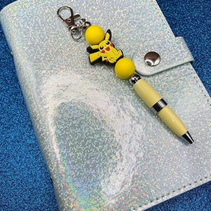 Yellow “Pikachu” character + round yellow silicone beads on pale yellow pen casing with black ink + clip. Write about your fave character.