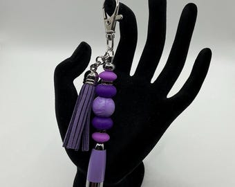Mini purple pen with black ink has clip and purple tassel with rhinestone spacers. Shades of purple silicone beads & light glittery pen.