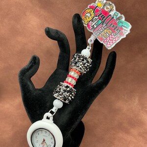 May include: White retractable badge reel with a black and red beaded chain and a white pocket watch. The badge holder features a colorful graphic with the text "Crafting Queen".
