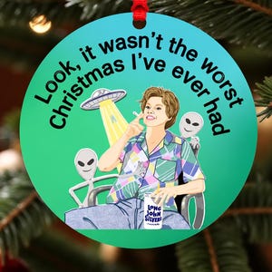 May include: A round green Christmas ornament featuring a graphic of a person in a plaid shirt holding a Long John Silver's cup, flanked by two gray aliens and a UFO. The text reads, Look, it wasn't the worst Christmas I've ever had.