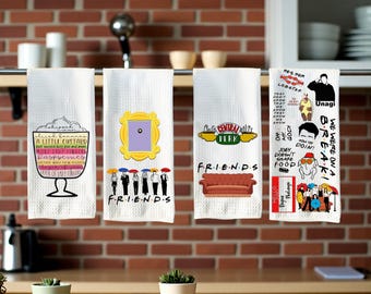 May include: Four white kitchen towels with different designs. One shows a custard dessert, another the Friends door frame, a third the Central Perk logo and sofa, and the last has quotes and characters from the TV show.