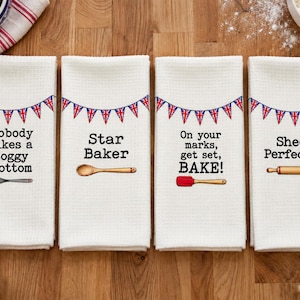 May include: Four white waffle-weave kitchen towels featuring a Union Jack bunting design. Each towel displays unique black text and a baking tool illustration: a whisk, a wooden spoon, a red spatula, and a wooden rolling pin.