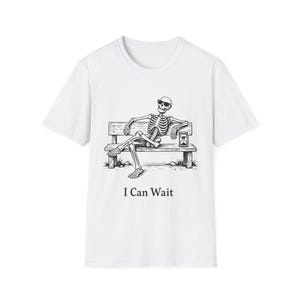 Puede incluir: Camiseta blanca con una ilustración en blanco y negro de un esqueleto con gafas de sol, descansando en un banco de parque con un reloj de arena. El texto "I Can Wait" está impreso debajo.