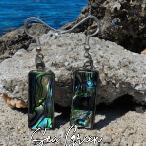 May include: A pair of rectangular drop earrings featuring iridescent abalone shell inlays with swirling green, blue, and black tones, encased in a thin silver-toned metal frame with standard hook-style ear wires and the text Sea Green.