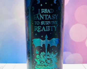May include: A tall, cylindrical tumbler with a teal and black gradient design. The tumbler features the text "I READ FANTASY TO SURVIVE REALITY" and illustrations of a dragon, open book, and hands. The overall theme is fantasy and reading.