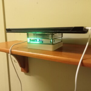 May include: A black tablet computer levitating above a white base with a green light. The base is on a wooden shelf with a white cord.