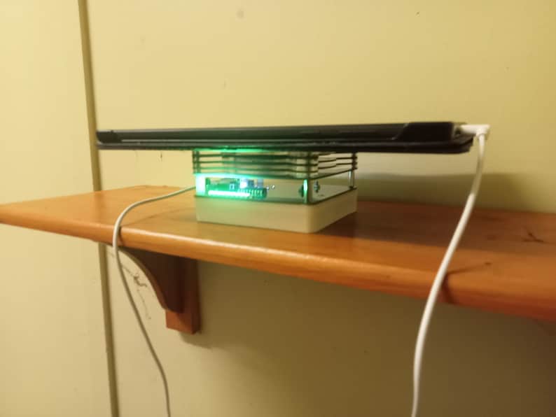 May include: A black tablet computer levitating above a white base with a green light. The base is on a wooden shelf with a white cord.