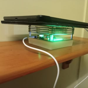 May include: A white charging stand with a clear plastic case and a green light. A black tablet is resting on top of the stand. A white charging cable is plugged into the stand.