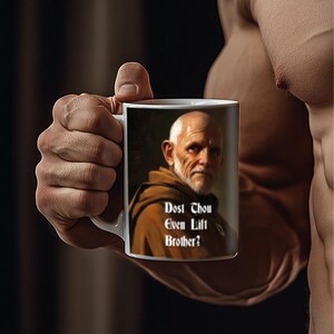 Pode incluir: Caneca de cerâmica branca com uma imagem de um homem com barba e uma túnica marrom. O texto na caneca diz "Dost Thou Even Lift Brother?"