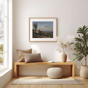May include: A framed landscape painting depicting a Tuscan villa scene with rolling hills, trees, and a blue sky. The artwork is displayed above a wooden bench with decorative pillows, a woven ottoman, and a potted plant, creating a cozy interior design.