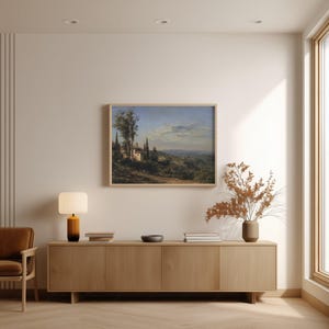 May include: A framed landscape painting depicts a Tuscan villa scene with rolling hills, trees, and a cloudy sky. The artwork hangs above a wooden cabinet with a lamp, books, and a vase with dried flowers.