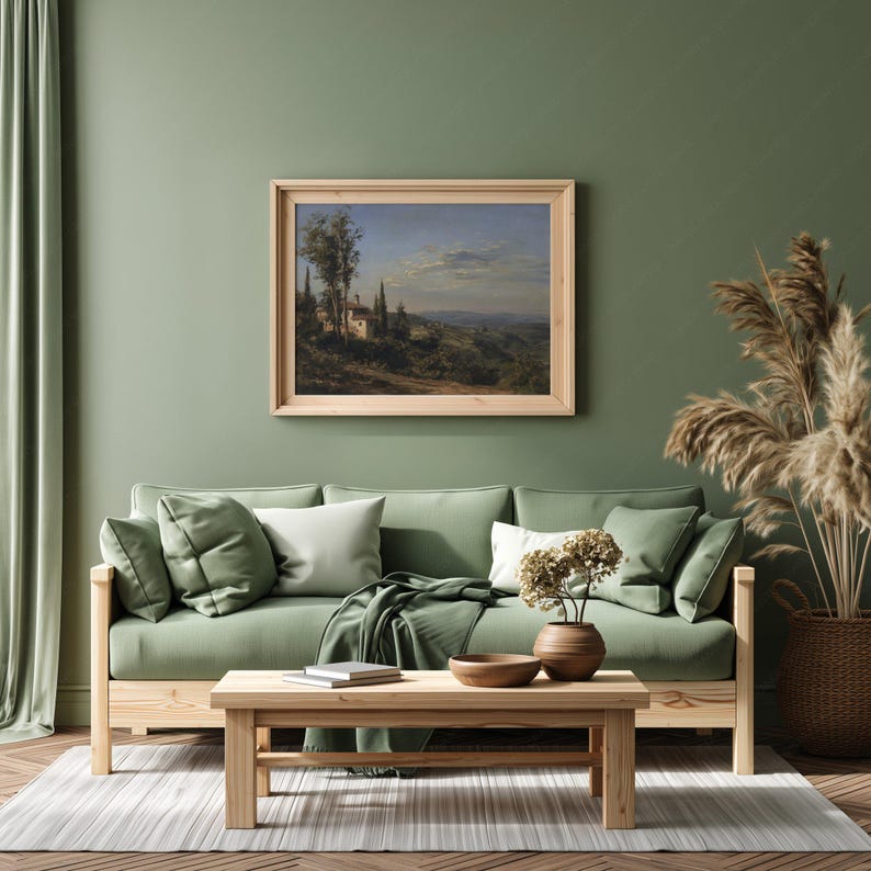May include: A living room scene with a green sofa, pillows, and a wooden coffee table. A framed landscape painting hangs above the sofa. Decorative elements include a woven basket with tall dried plants and a vase with dried flowers.