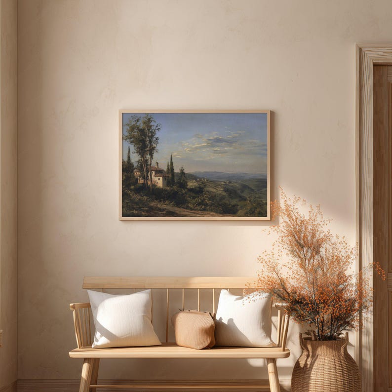 May include: A framed landscape painting depicts a serene Italian countryside scene. The artwork features a villa, cypress trees, and rolling hills under a blue sky with clouds. The painting is displayed above a wooden bench with pillows and a woven vase with dried plants.
