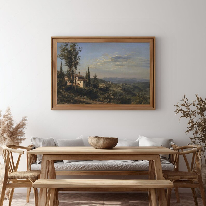 May include: A framed landscape painting depicts a Tuscan scene with a white building, trees, and rolling hills under a blue sky. The artwork is displayed in a natural wood frame, adding a touch of rustic elegance to the room.
