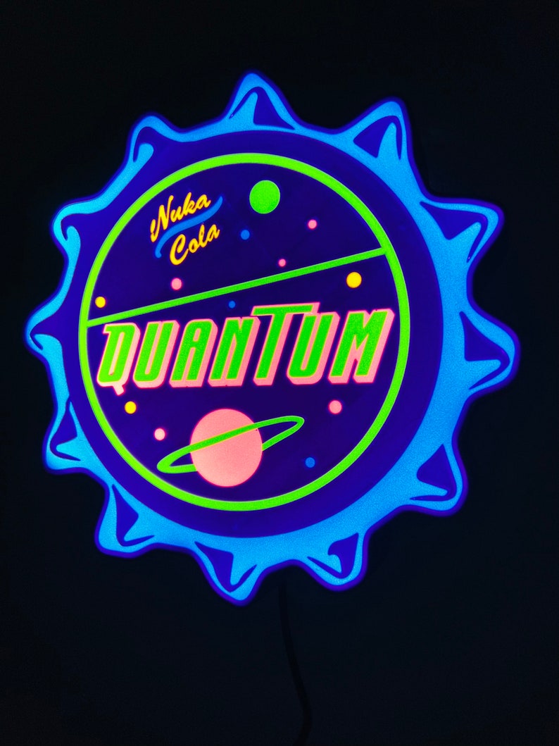 May include: A neon sign in the shape of a bottle cap, featuring the words "Nuka Cola Quantum" in yellow and green. The sign has a blue and green color scheme with a planet graphic. The sign is against a black background.