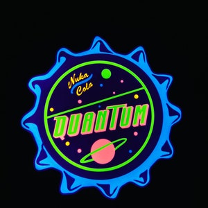May include: A circular Nuka Cola Quantum design with a blue, green, and pink color scheme. The design features the words "Nuka Cola" and "Quantum" in a retro font, with a planet and stars.