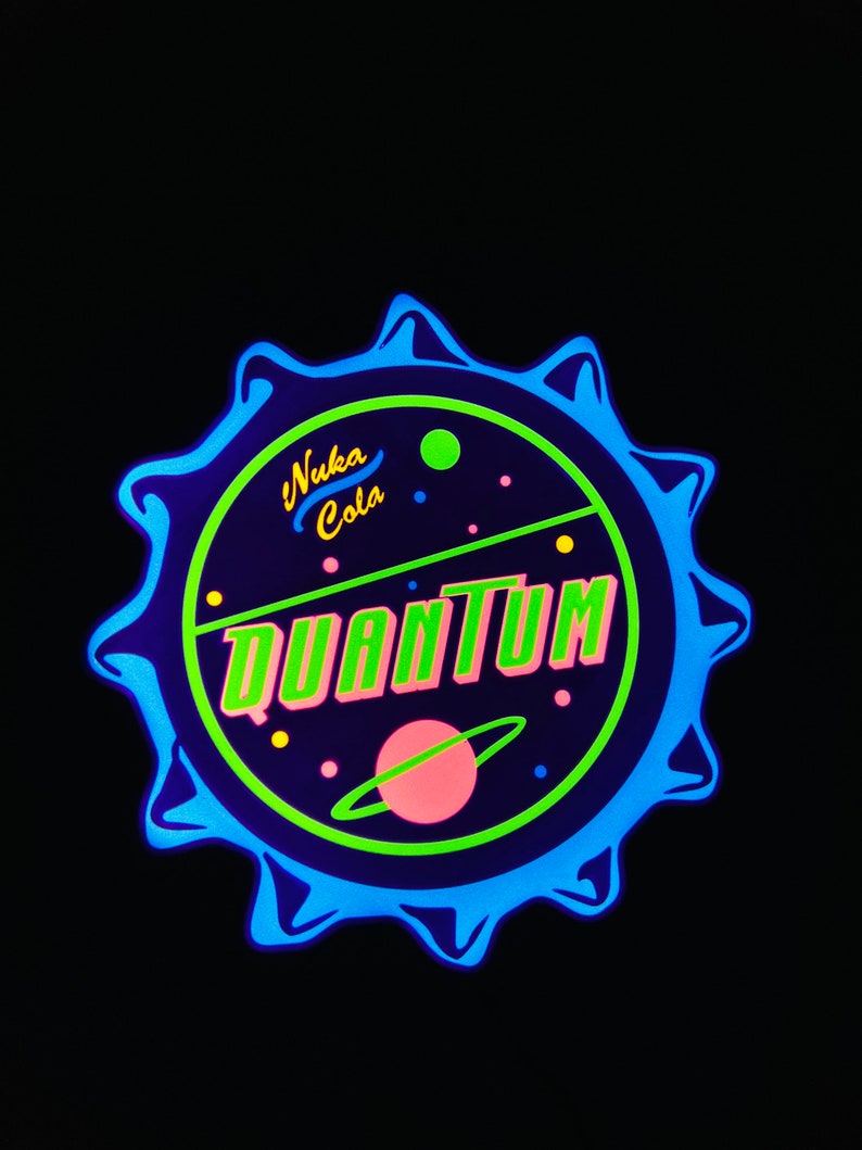 May include: A circular Nuka Cola Quantum design with a blue, green, and pink color scheme. The design features the words "Nuka Cola" and "Quantum" in a retro font, with a planet and stars.