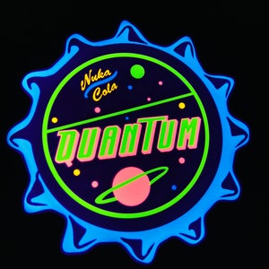 May include: A neon sign in the shape of a bottle cap, featuring the words "Nuka Cola Quantum" in green and pink. The design includes a planet with rings and various colored dots, all set against a dark background with a blue outline.