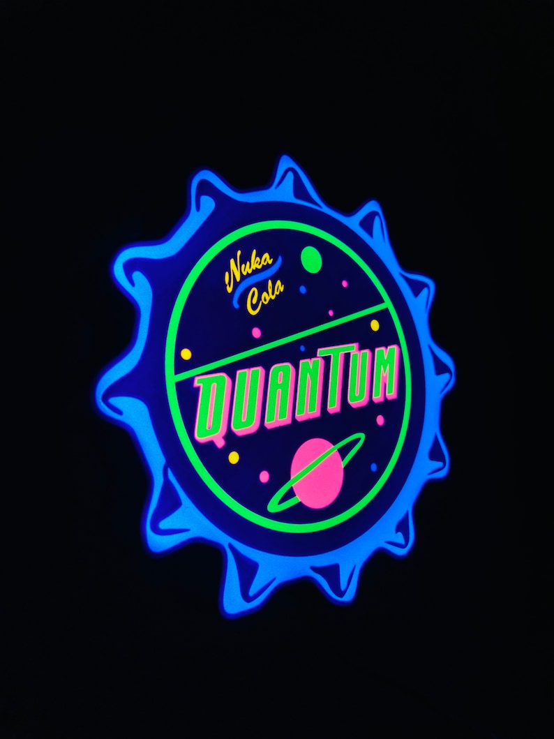 May include: A glowing, circular sign with a blue, bottle cap-like edge. The sign features the words "Nuka Cola Quantum" in neon green and pink, with a planet graphic. The background is black.