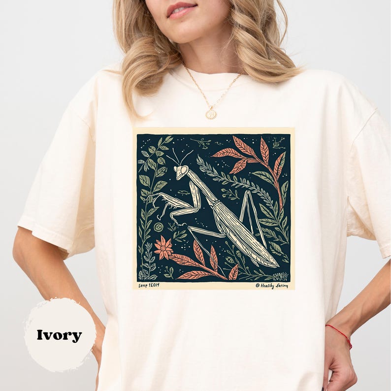 May include: Ivory-colored t-shirt featuring a detailed illustration of a praying mantis within a square frame. The artwork includes botanical elements in shades of green, orange, and cream against a dark blue background. The text "Semp 16014" and "@Healthy daring" are visible.