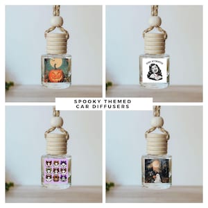 May include: Four glass car diffusers with wooden caps and hanging ropes. Each bottle features a unique graphic: a jack-o'-lantern, a woman with the text STAY HYDRATED, a grid of nine stylized cat faces, and a ghost in a forest with a full moon.