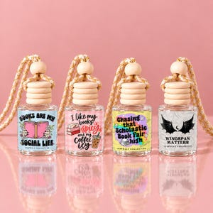 May include: Four glass car air freshener bottles with wooden caps and hanging cords. The first label reads 'BOOKS ARE MY SOCIAL LIFE', the second 'I LIKE MY BOOKS SPICY AND MY COFFEE ICY', the third 'CHASING THAT SCHOLASTIC BOOK FAIR HIGH', and the fourth 'WINGSPAN MATTERS'.