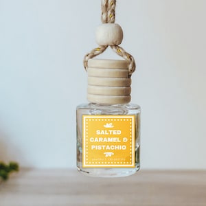 May include: A clear glass bottle with a wooden cap and a yellow label that reads "Salted Caramel & Pistachio" hanging from a brown string. The bottle is a car air freshener.