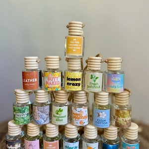May include: A collection of 18 small glass bottles with wooden tops and colorful labels. The bottles contain scented oils and are designed to be hung in a car. The labels feature various scents, including leather, salted caramel, and fresh patchouli.