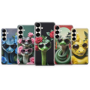 May include: Five smartphone cases featuring snakes wearing sunglasses. The first is blue with blue roses, the second shows two snakes with pink glasses and pink roses, the third is black with a green snake and red roses, the fourth is green with a coiled snake, and the fifth is yellow with sunflowers.