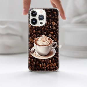 May include: A clear phone case with a coffee-themed design. The case displays a pattern of coffee beans and a cup of coffee topped with whipped cream. The phone case is held by a hand.