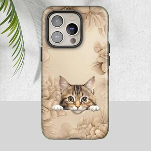 May include: A phone case with a tabby cat design, framed by sepia-toned flowers. The case has a green border and a beige background. The cat has brown and tan stripes and large eyes, peeking over the floral border.